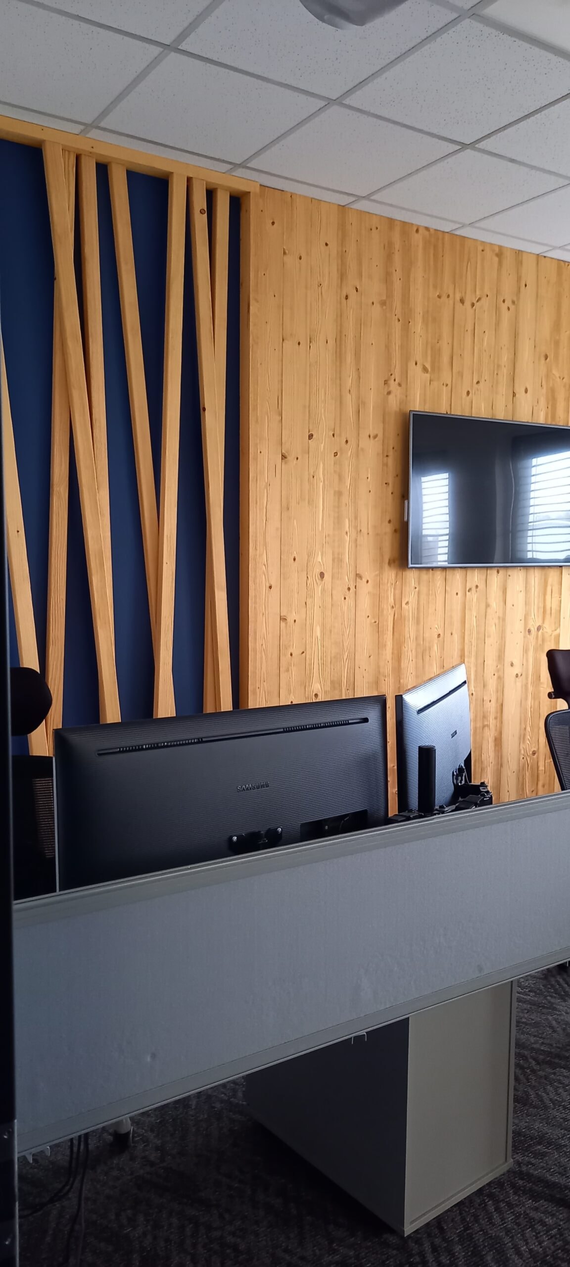 Pracovní místa s monitory za dělicí příčkou a obrazovkou na dřevěné stěně