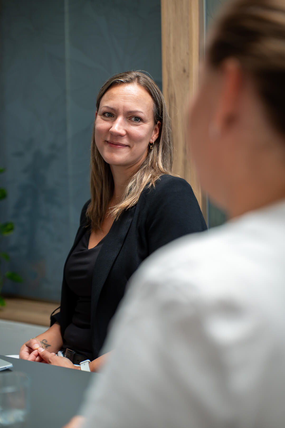 Žena v černém saku sedí u jednacího stolu a naslouchá ženě naproti
